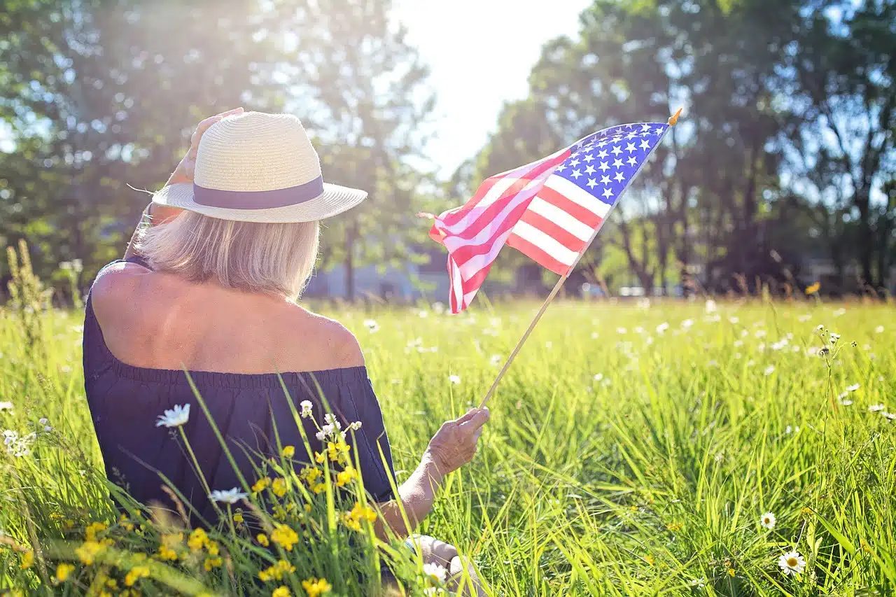 דוברת שפת אם אנגלית יושבת על דשא ומחזיקה דגל ארצות הברית